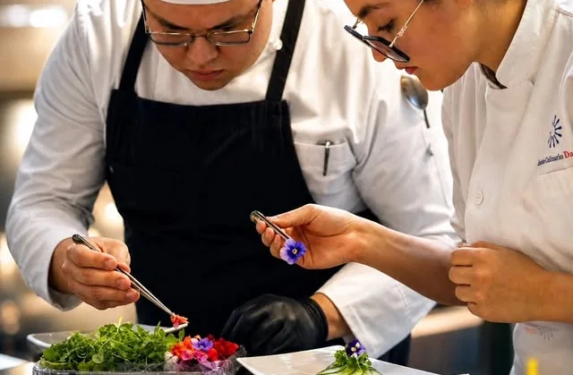 Dos alumnos del Instituto Culinario Danieli emplatando con pinzas y flores comestibles